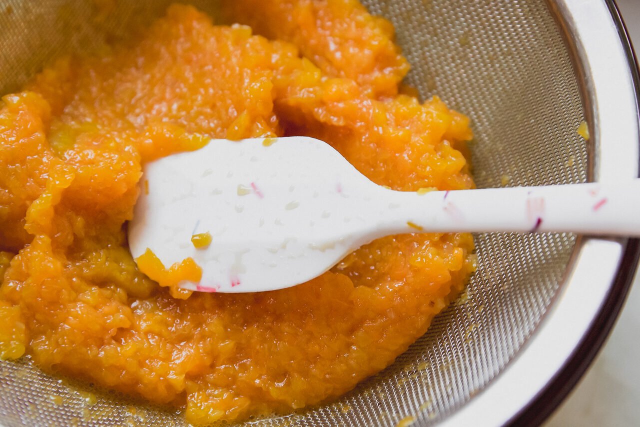 Peach pulp straining with a fine mesh strainer.