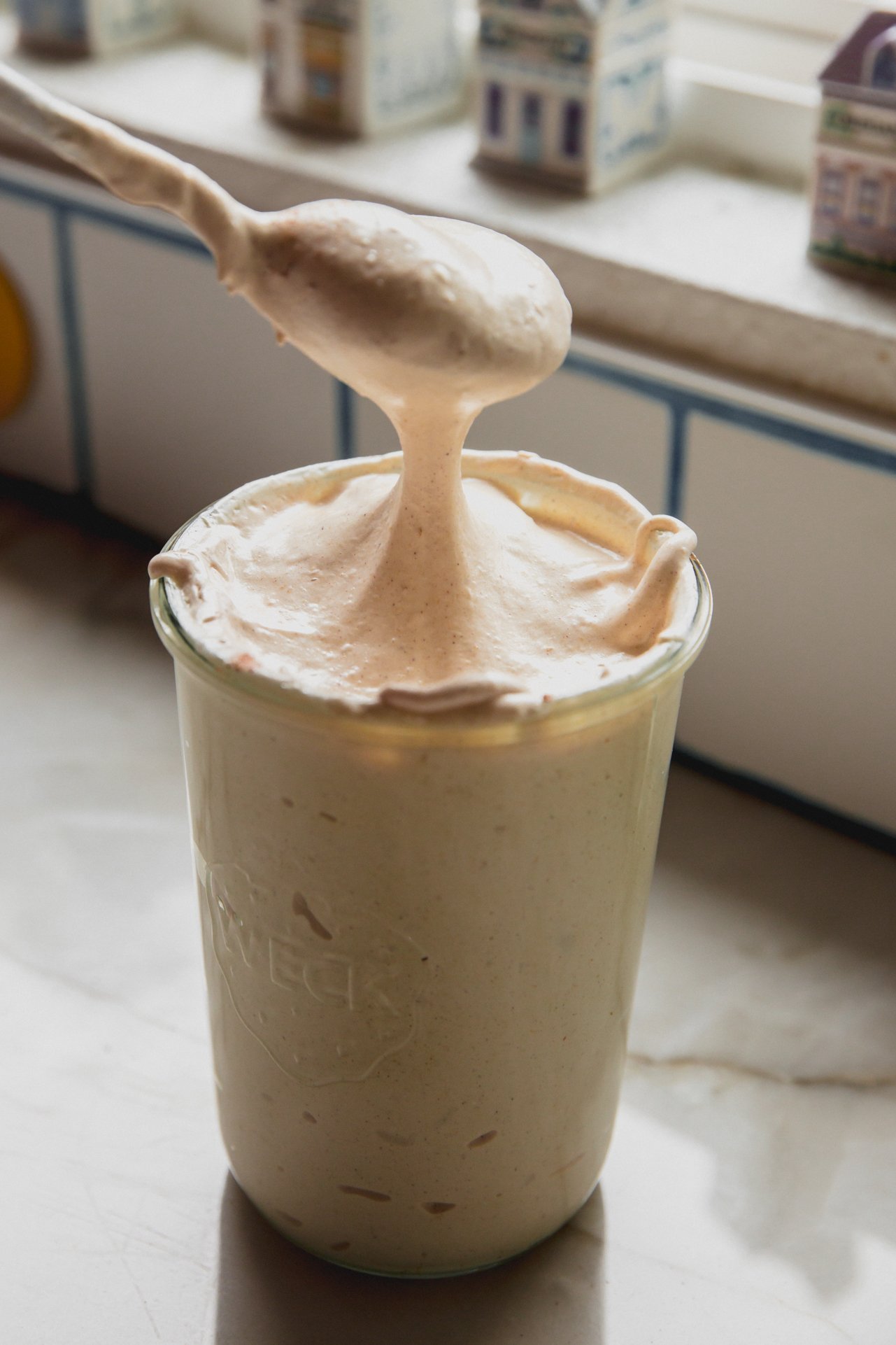 A spoon putting pumpkin pie marshmallow fluff into a glass jar.