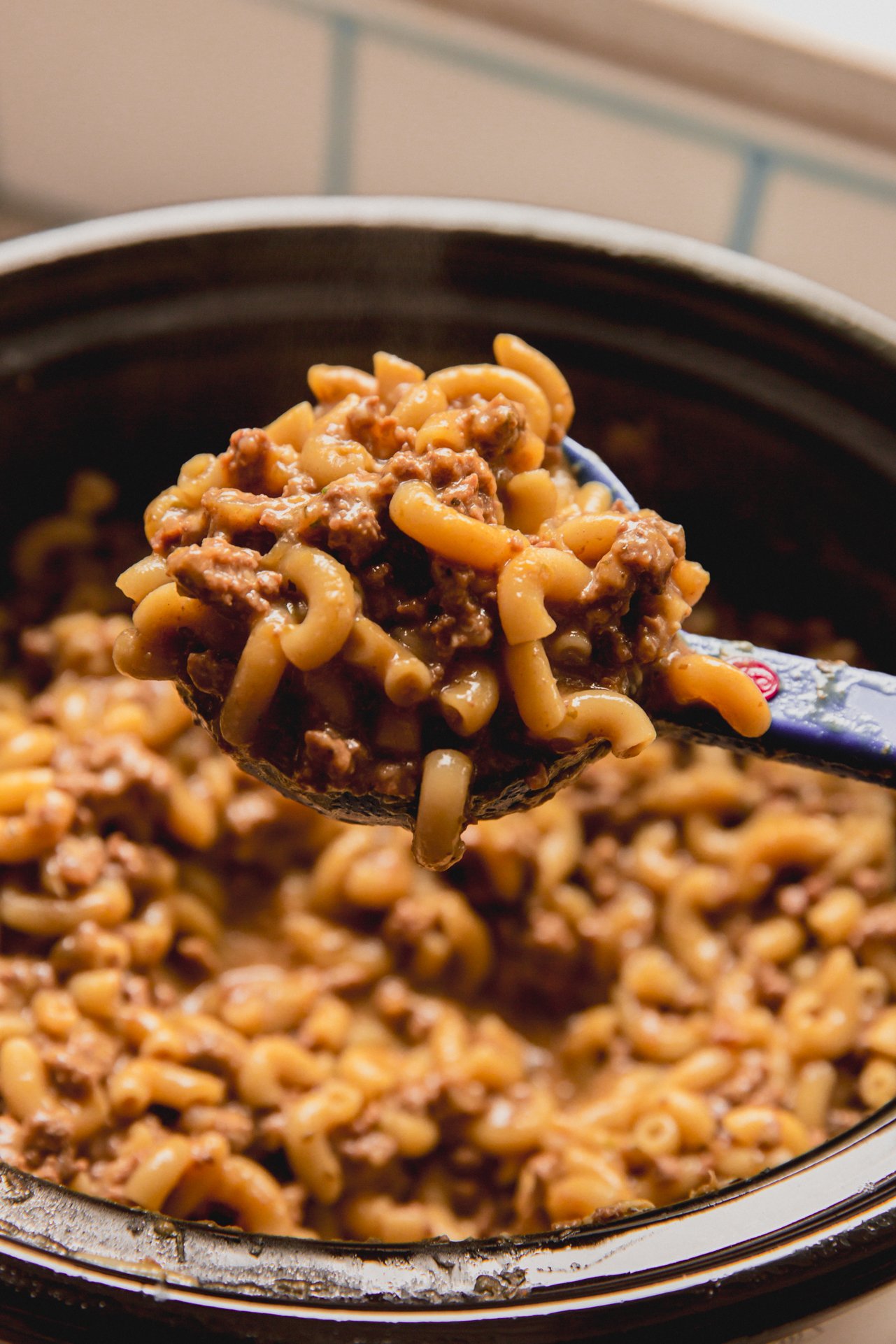 A spoon lifting a scoop of slow cooker hamburger helper out of the slow cooker.