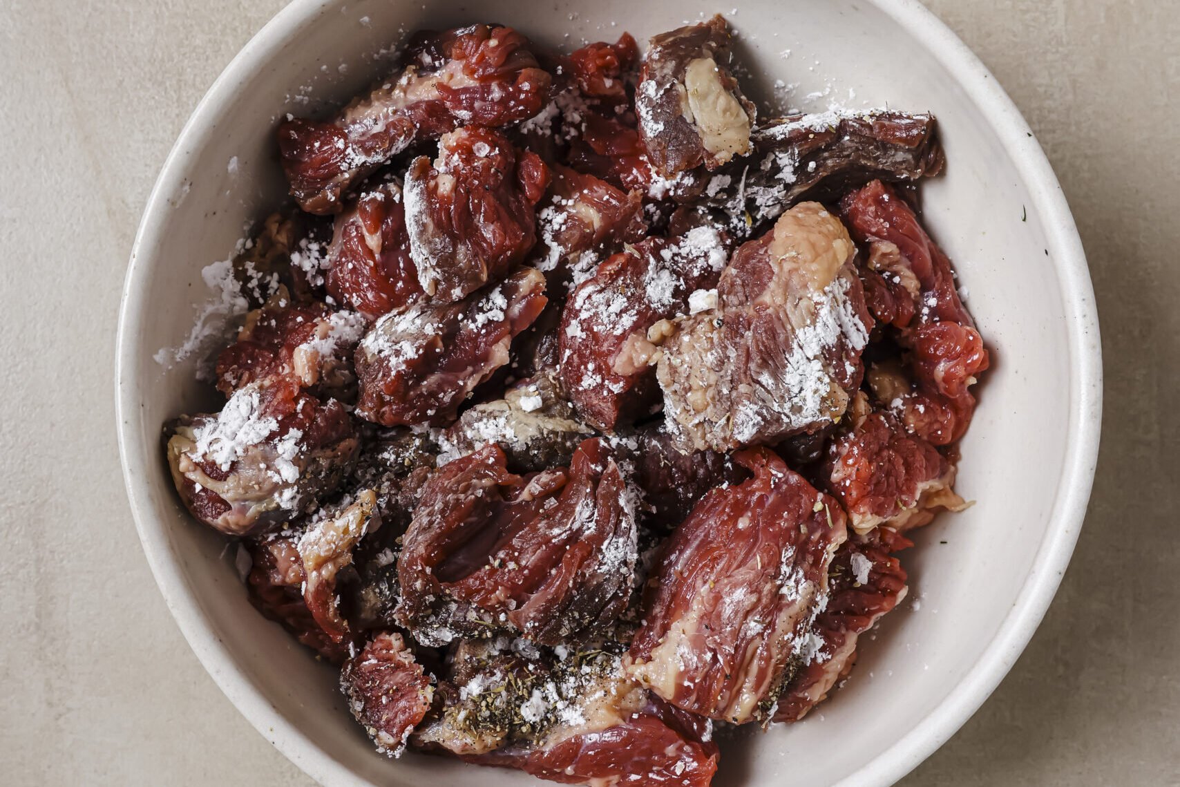 Beef stew meat being tossed with arrowroot starch.