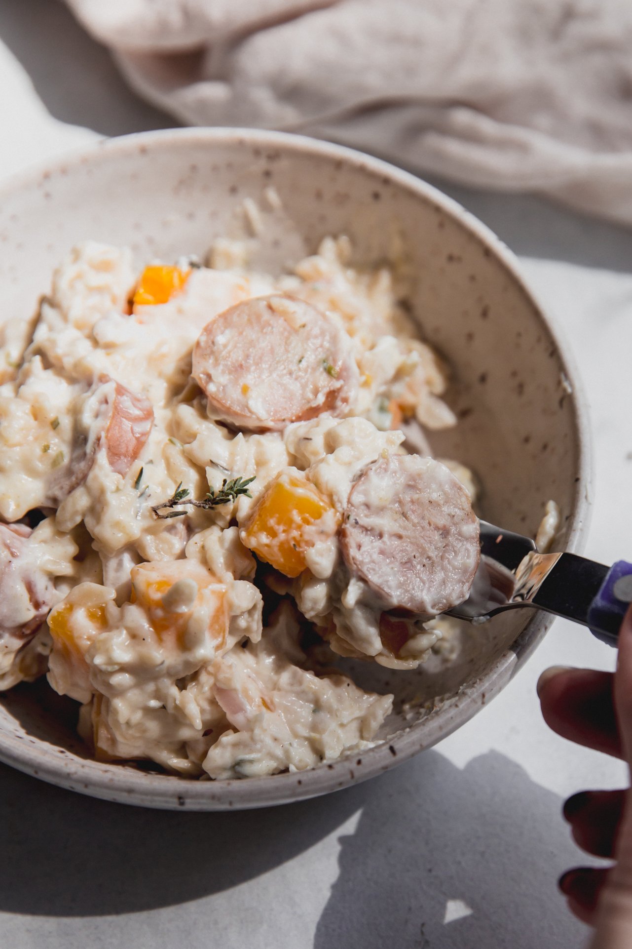 A bowl of chicken sausage and orzo with a spoon taking a bite out.