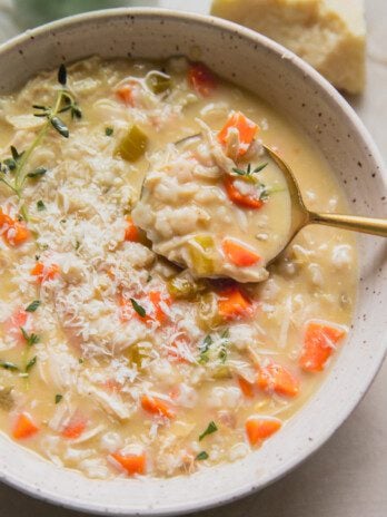 Pastina chicken soup topped with thyme and cheese with a spoon.