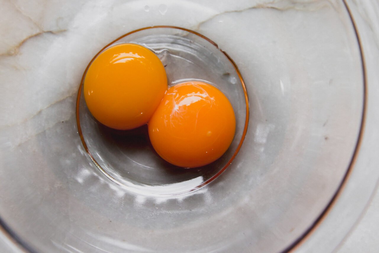 Two egg yolks in a class bowl before mixing.