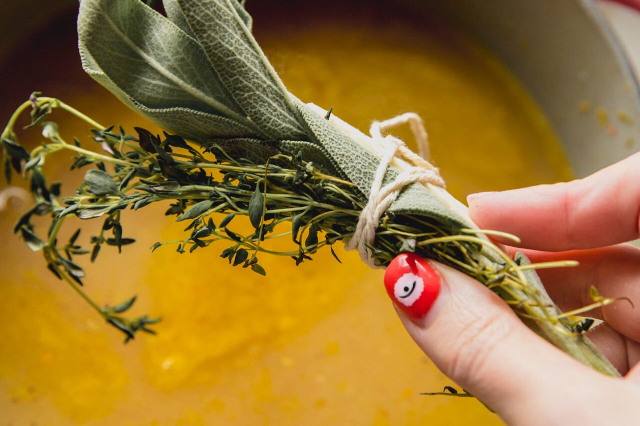 A hand with a bundle of herbs adding to the soup.