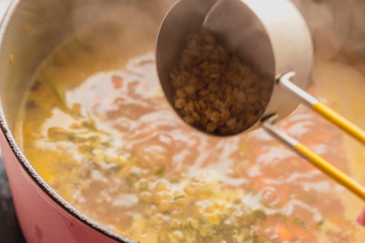 A measuring cup adding the pasta to the soup.