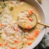 Pastina chicken soup topped with thyme and cheese with a spoon.