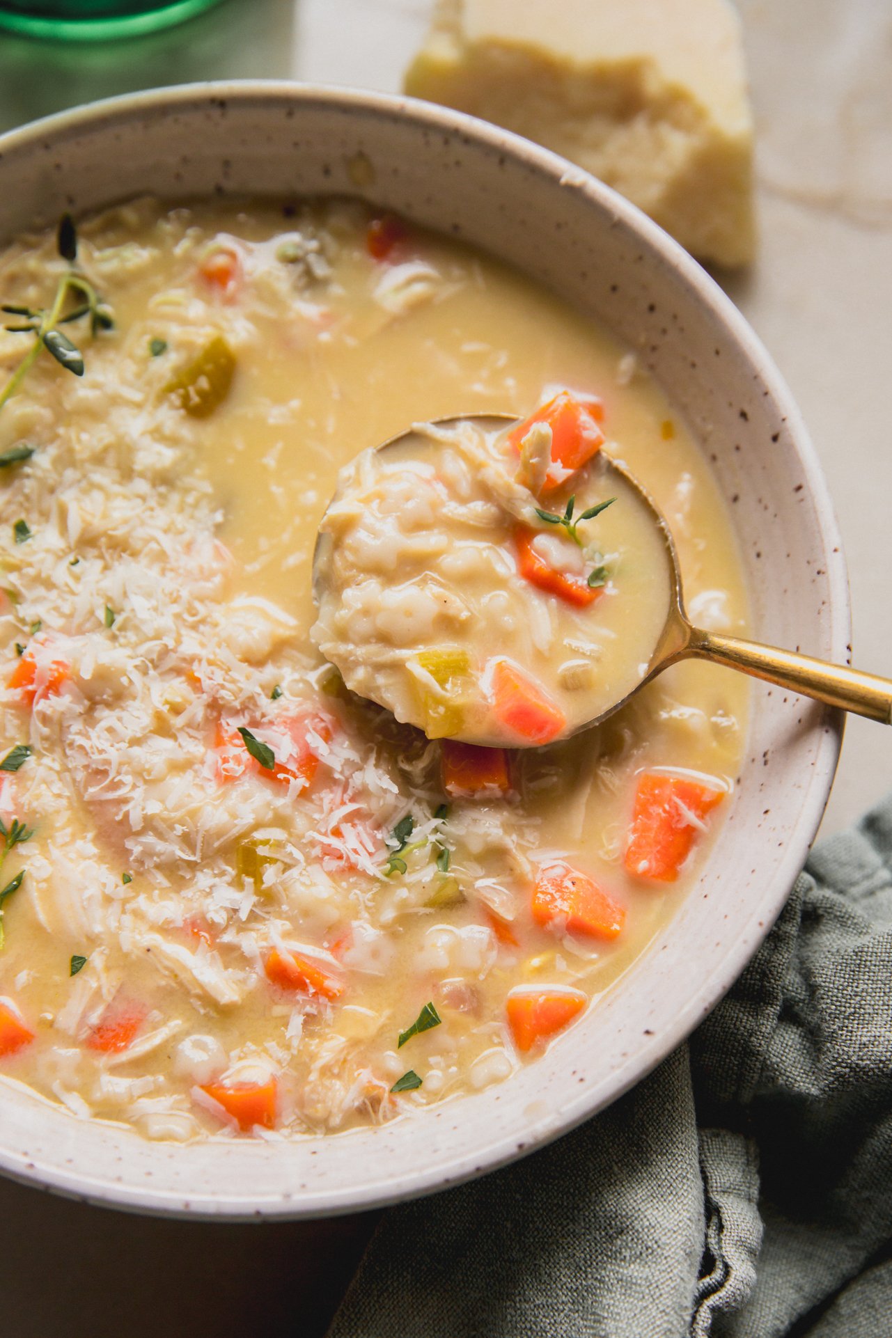 Pastina chicken soup topped with thyme and cheese with a spoon.