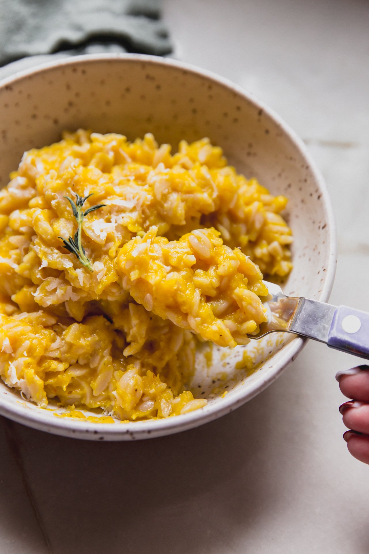 A spoon taking a bite of pumpkin orzo out of a bowl.