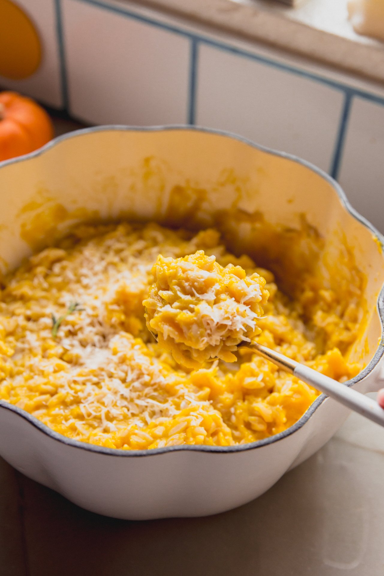 A spoon taking a taking a spoonful of pumpkin orzo out of a serving dish of it.