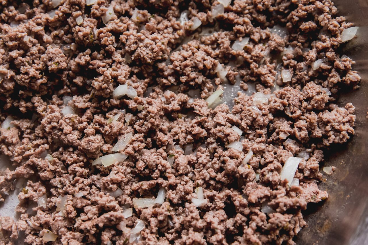 Ground beef browning in a pan with onion.
