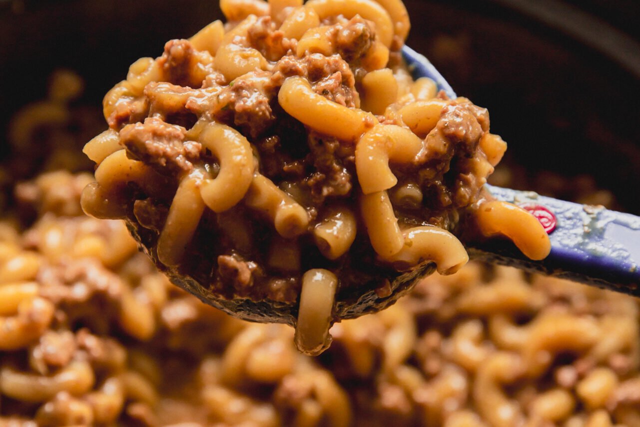 A serving spoon taking a scoop of slow cooker hamburger helper out.