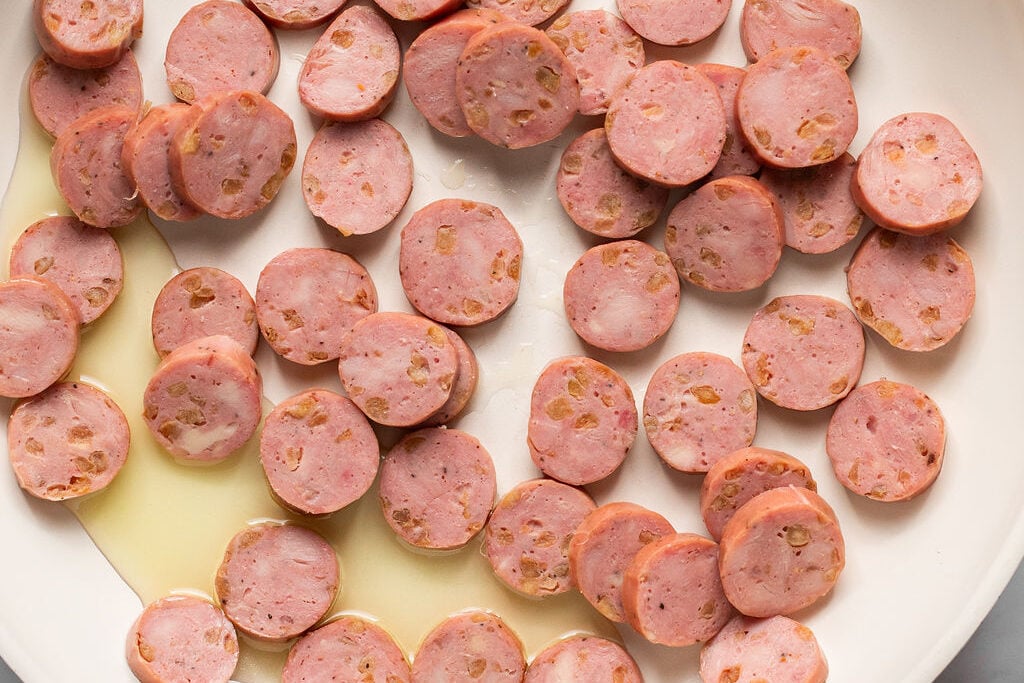Sliced chicken sausage uncooked in a pan.