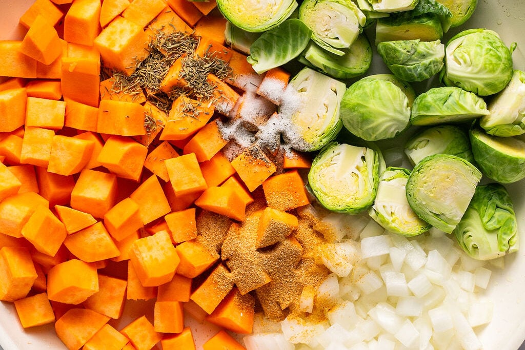 Uncooked sweet potato, brussels and onion in pan.