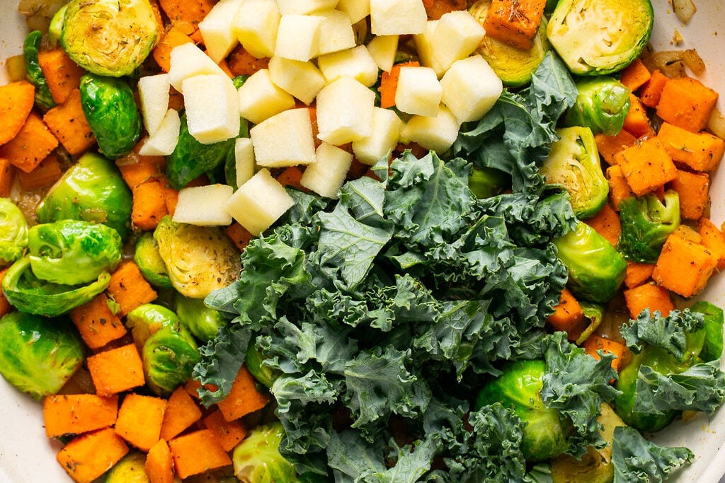 Cooked sweet potato, brussels and onion in pan.