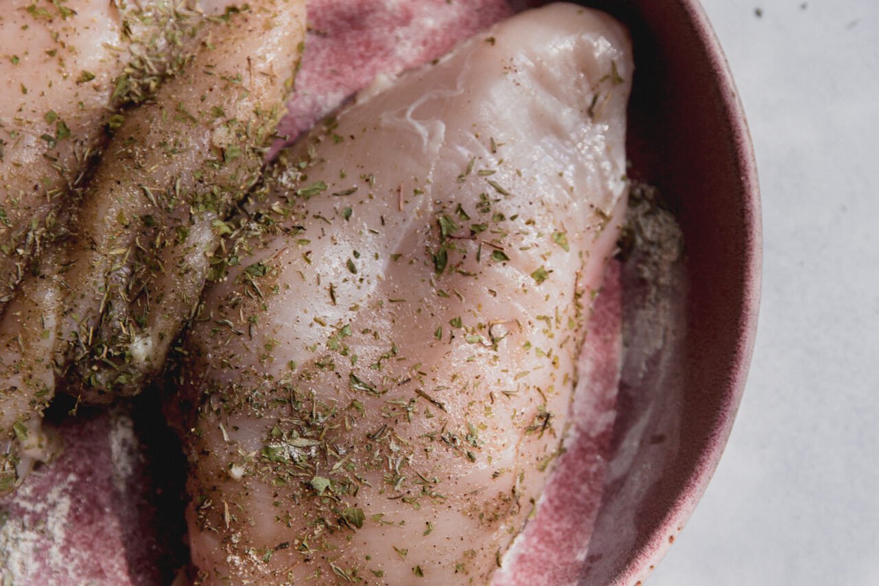 Chicken in a bowl seasoned with herbs.