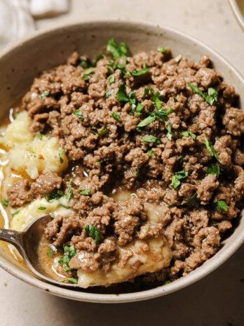 Ground beef and gravy served over mashed potatoes in a bowl.