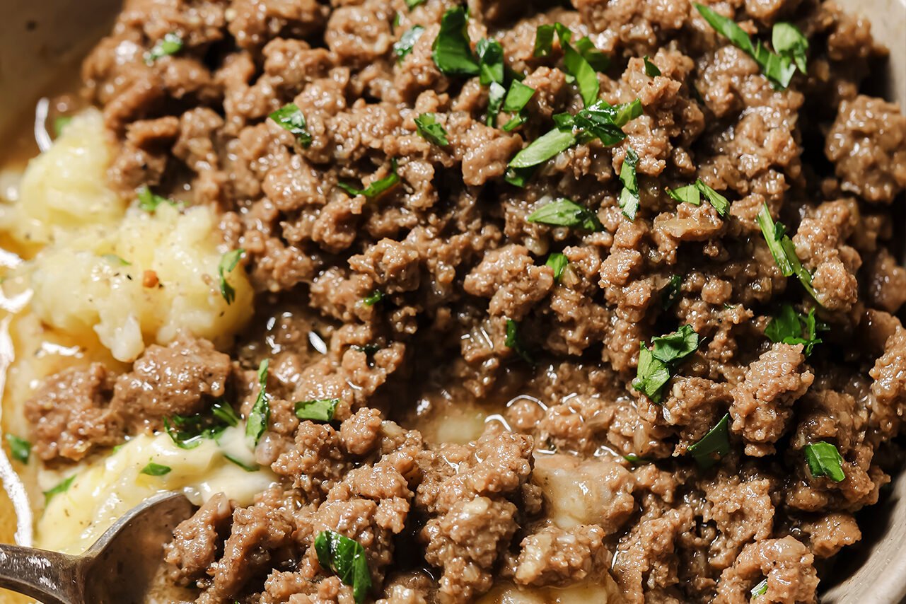 Ground beef and gravy served over mashed potatoes in a bowl.