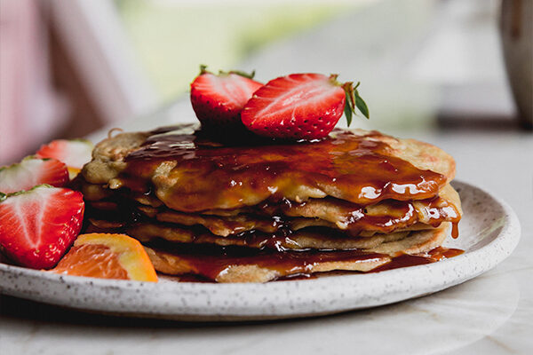 Pancakes with orange syrup and a strawberry on top.