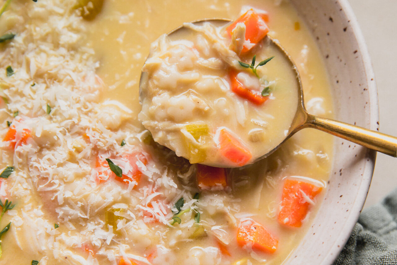 Pastina chicken soup topped with thyme and cheese with a spoon.