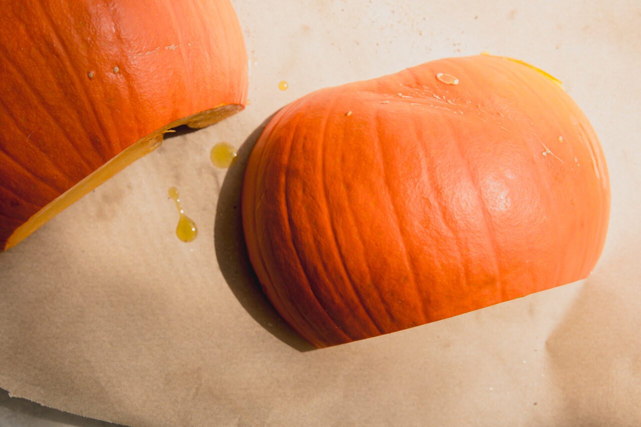A sugar pumpkin cut in half and face down on a baking sheet.