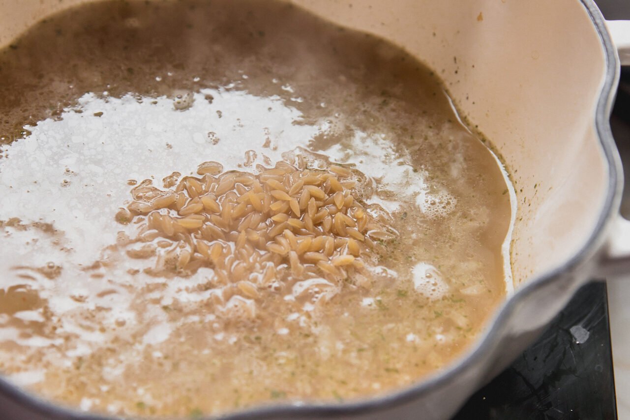 A pot with orzo and liquid ingredients cooking.
