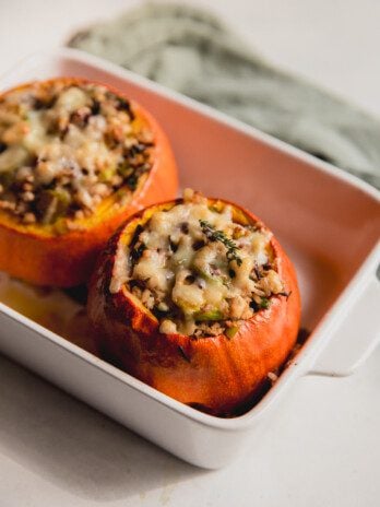 Two roasted stuffed pumpkins in a baking dish.