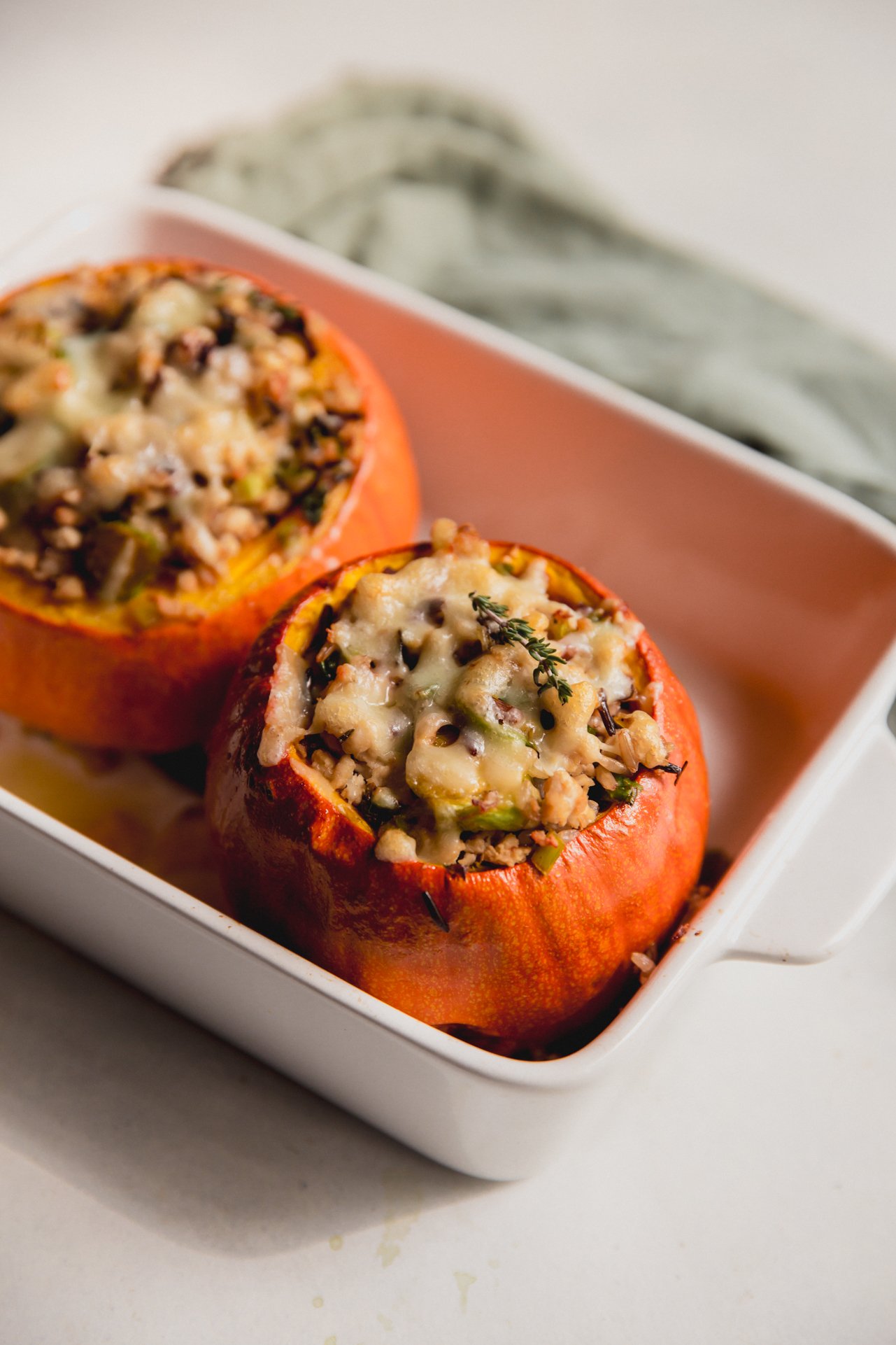 Two roasted stuffed pumpkins in a baking dish.