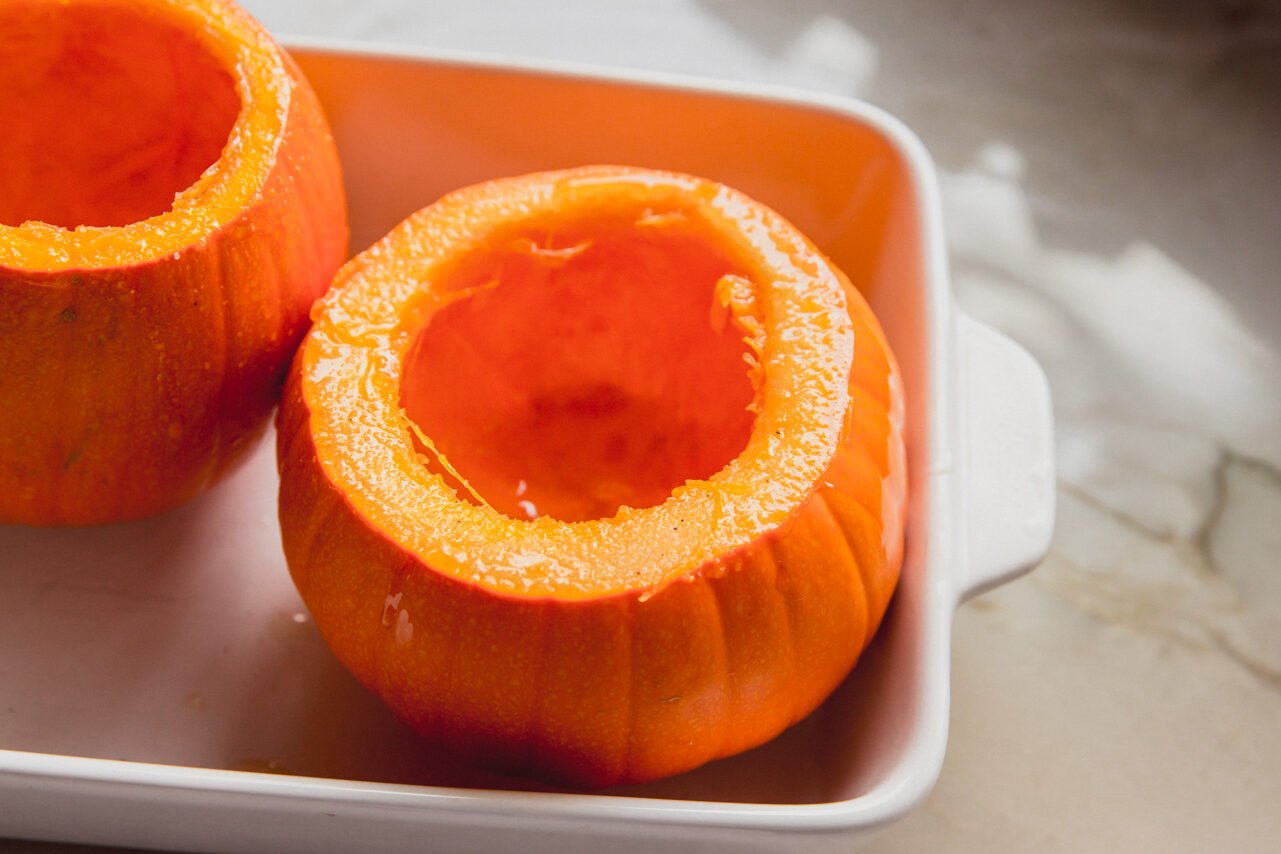 Pumpkins uncooked with the tops cut off in a baking dish.