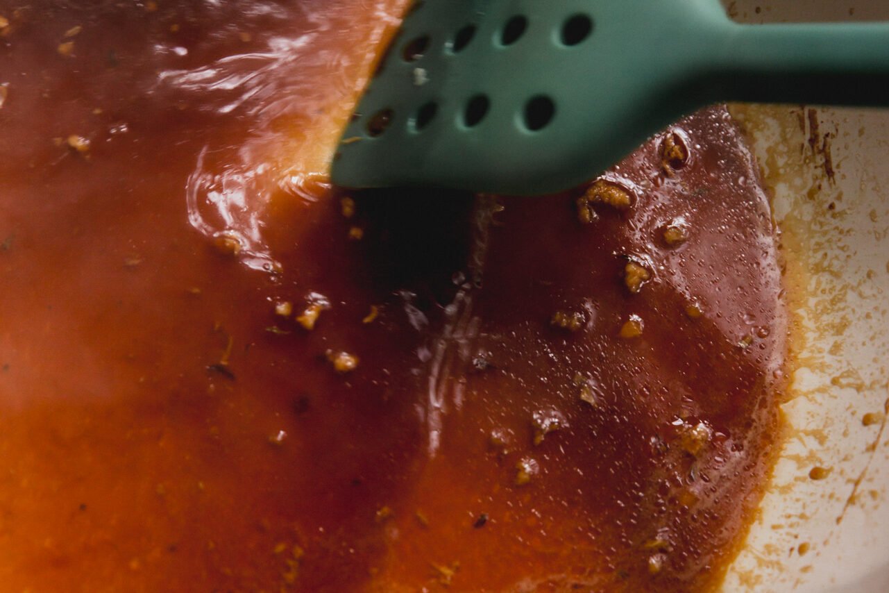 Orange glaze in a pan being stirred. 