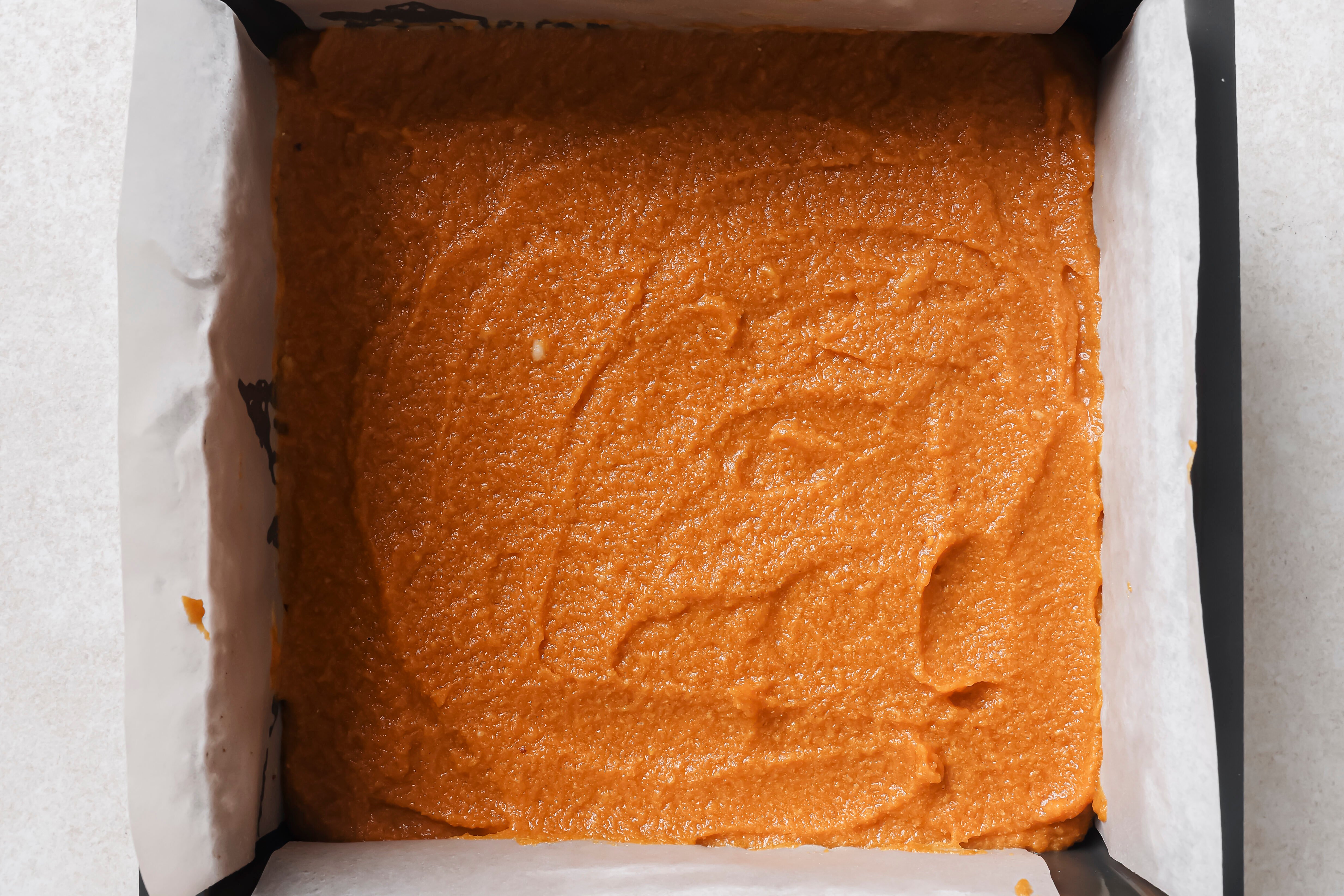 Pumpkin pie bar filling over the crust in a baking pan, ready to be set in the fridge.