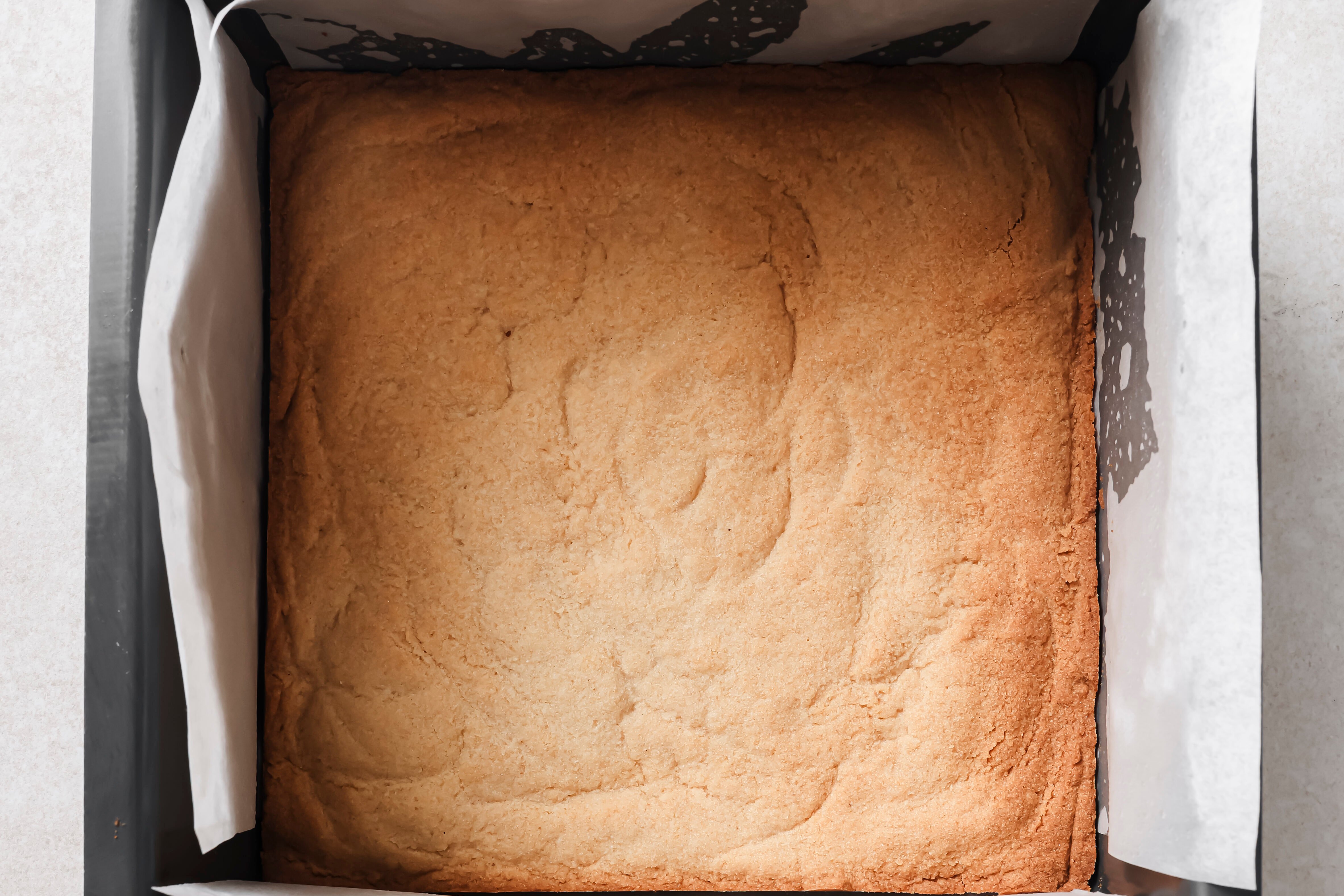 Pumpkin pie bar crust baked in a baking pan with parchment paper.