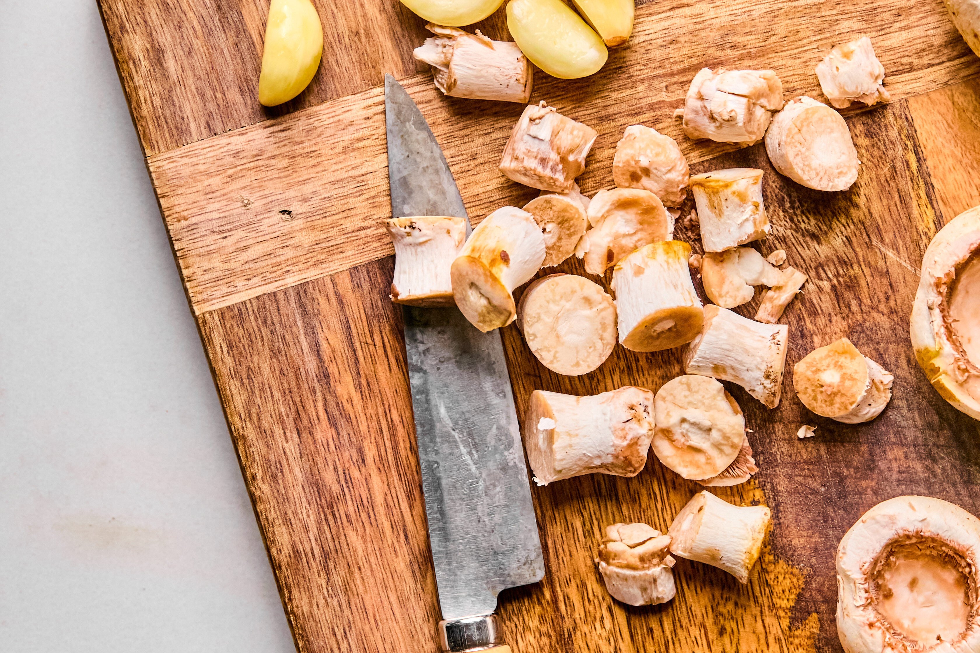 A cutting board with garlic and mushroom stems on it after slicing. 