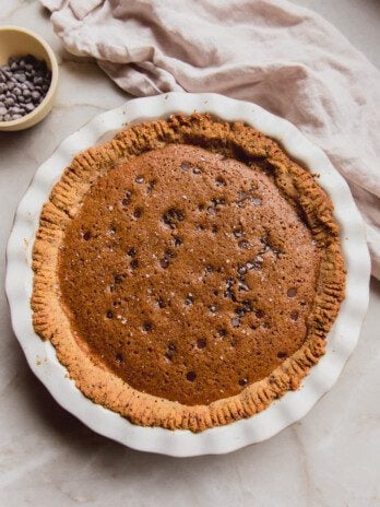 Chocolate chip cookie pie in a large white pan pan with a bowl of chocolate chips on the side.