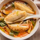 Gluten free potsticker soup in a bowl with a spoon scooping a potsticker out.