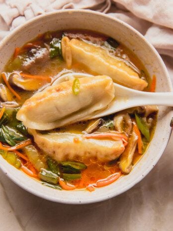 Gluten free potsticker soup in a bowl with a spoon scooping a potsticker out.