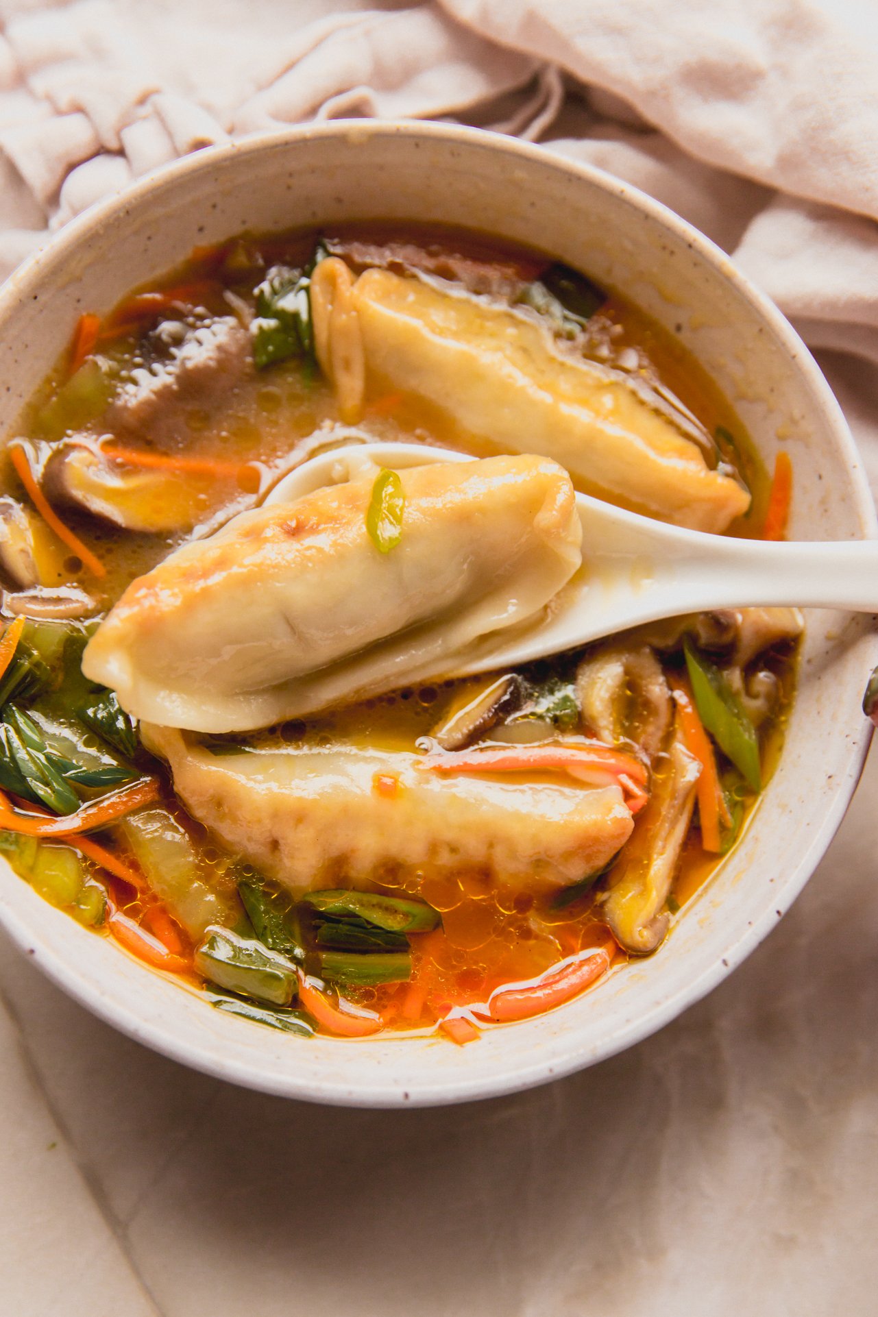 Gluten free potsticker soup in a bowl with a spoon scooping a potsticker out.