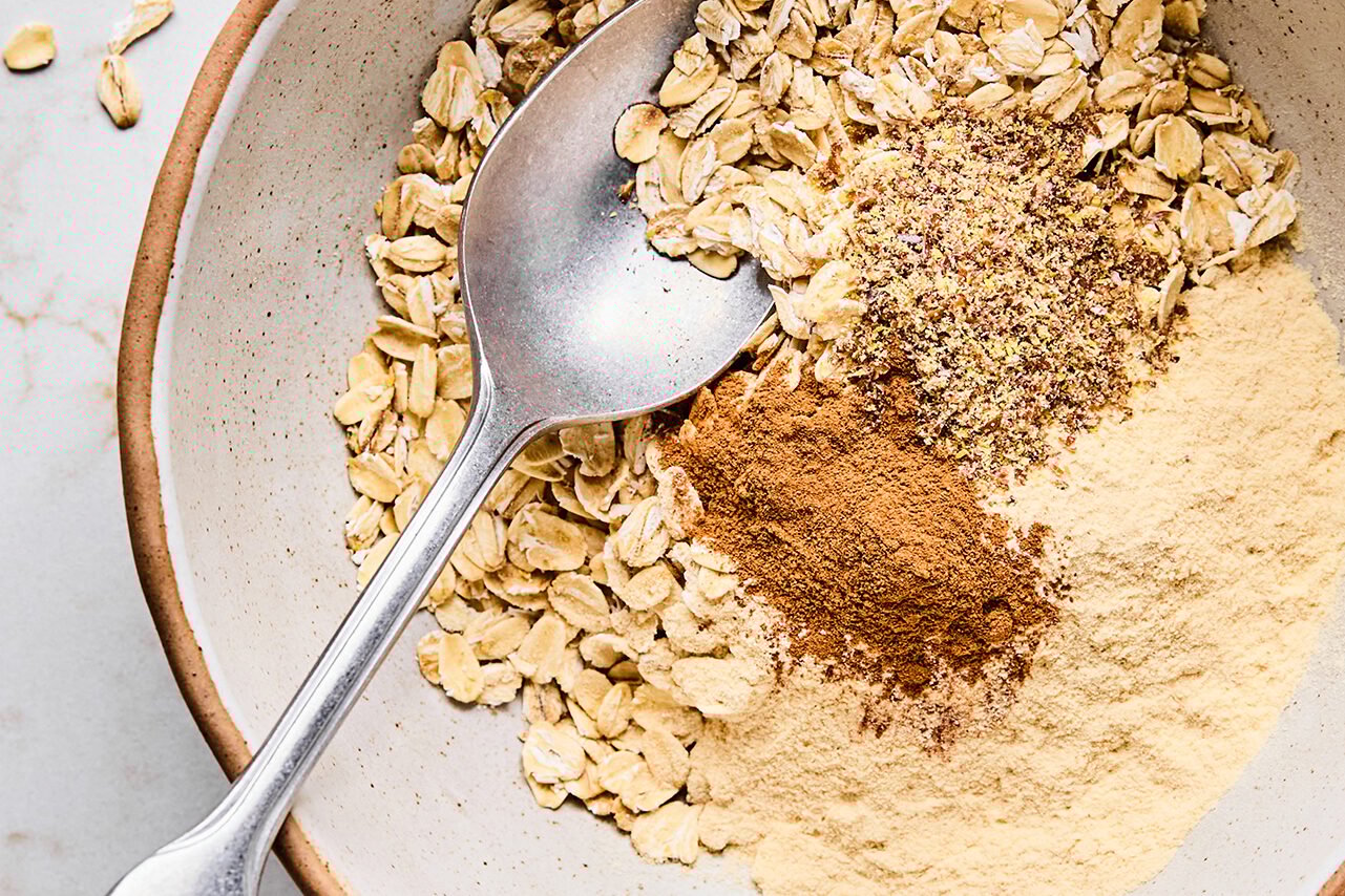 The oats, cinnamon, protein powder, and flax in a bowl with a spoon before mixing.