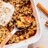 Protein apple crisp in a baking dish with a spoon taking a small serving.