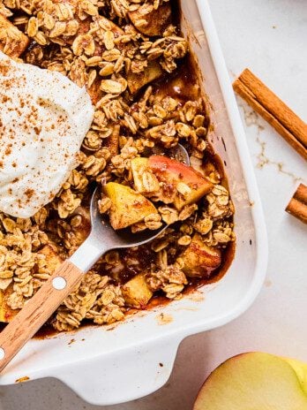 Protein apple crisp in a baking dish with a spoon taking a small serving.