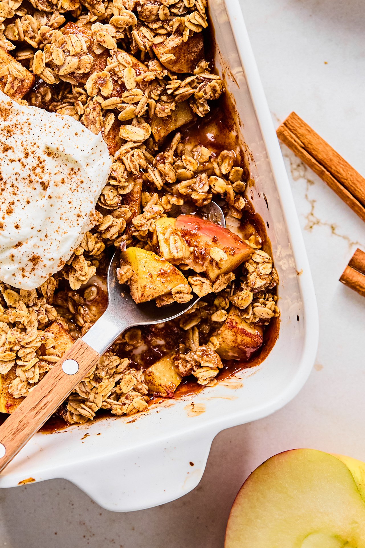 Protein apple crisp in a baking dish with a spoon taking a small serving.