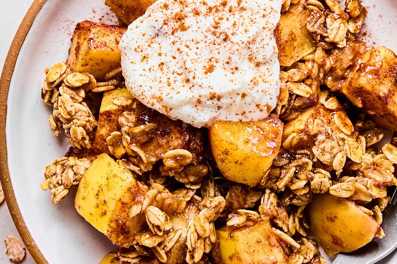 A serving of protein apple crisp on a plate topped with cinnamon and yogurt.
