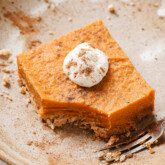 One pumpkin pie bar on a plate topped with coconut cream and cinnamon.