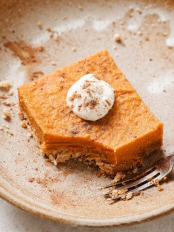 One pumpkin pie bar on a plate topped with coconut cream and cinnamon.