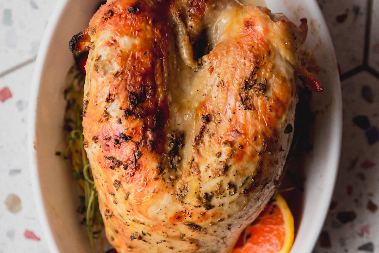 The turkey breast in a white ceramic bowl with greens and orange slices around it.