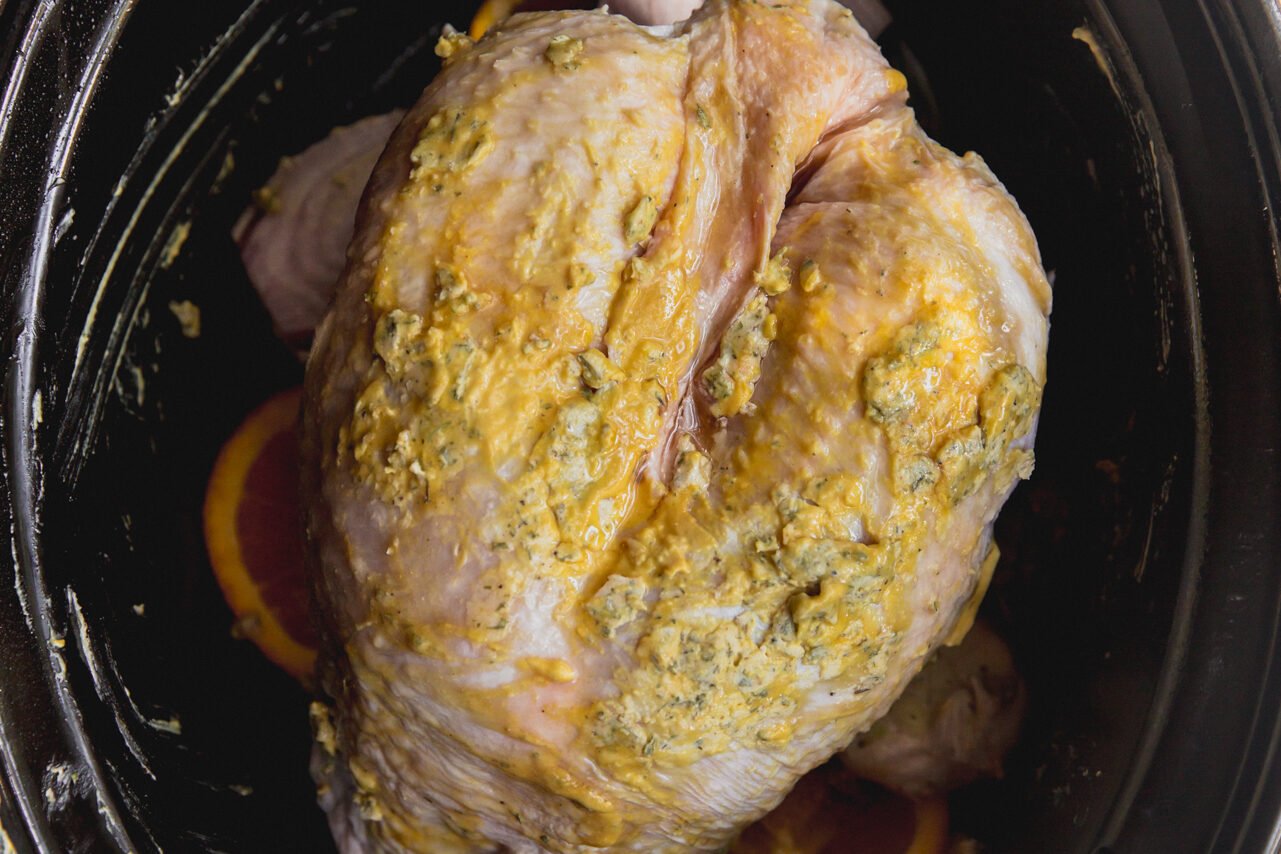 The raw turkey breast with ghee and mustard on it in a slow cooker before cooking.