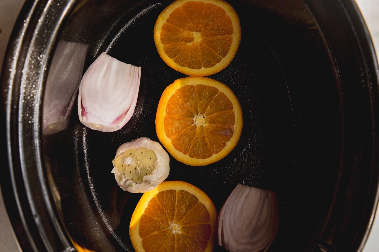 The slow cooker with orange slices, garlic and shallot in it.
