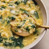 Stracciatella soup in a bowl with a large spoon.