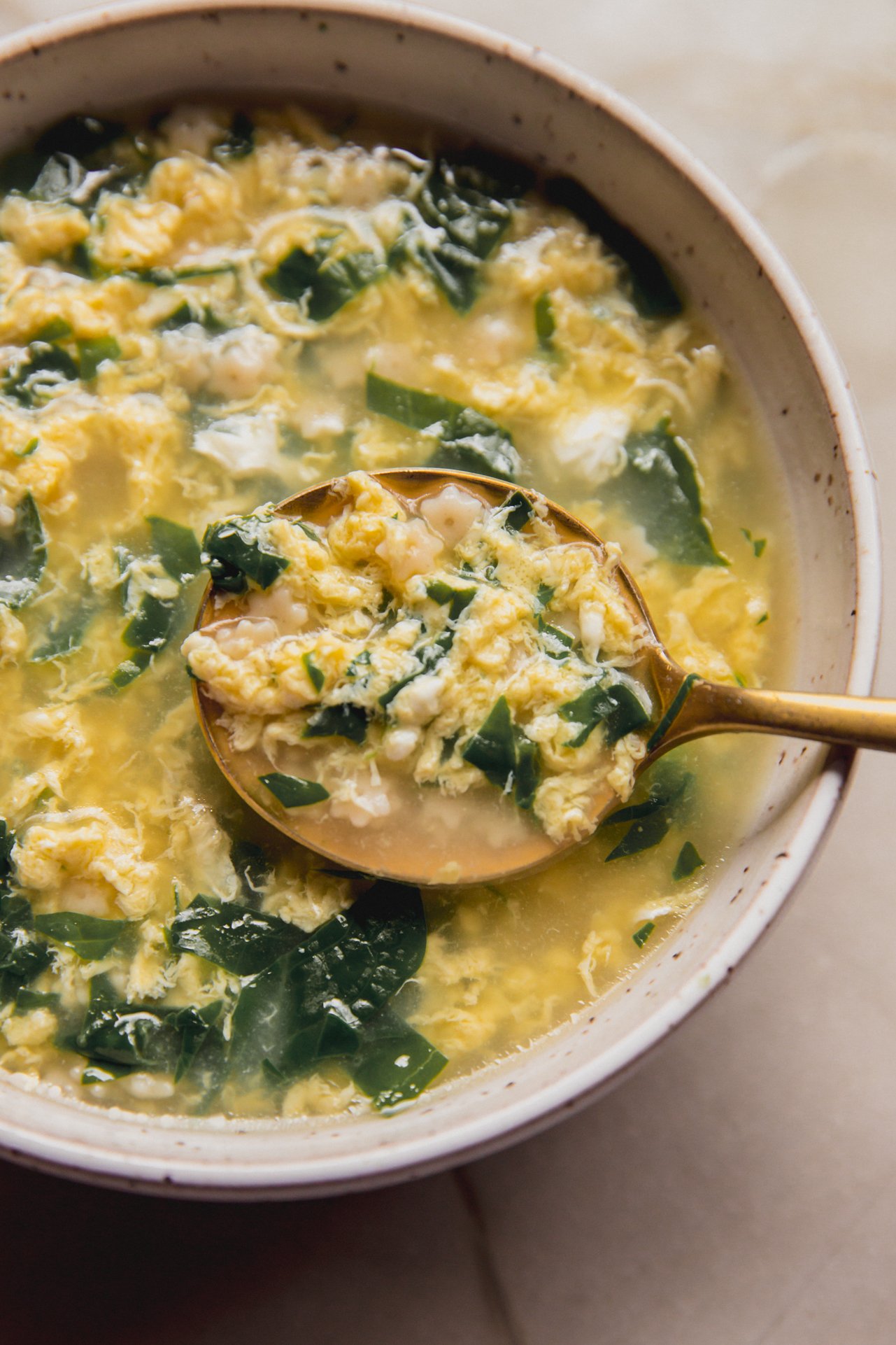 Stracciatella soup in a bowl with a large spoon.