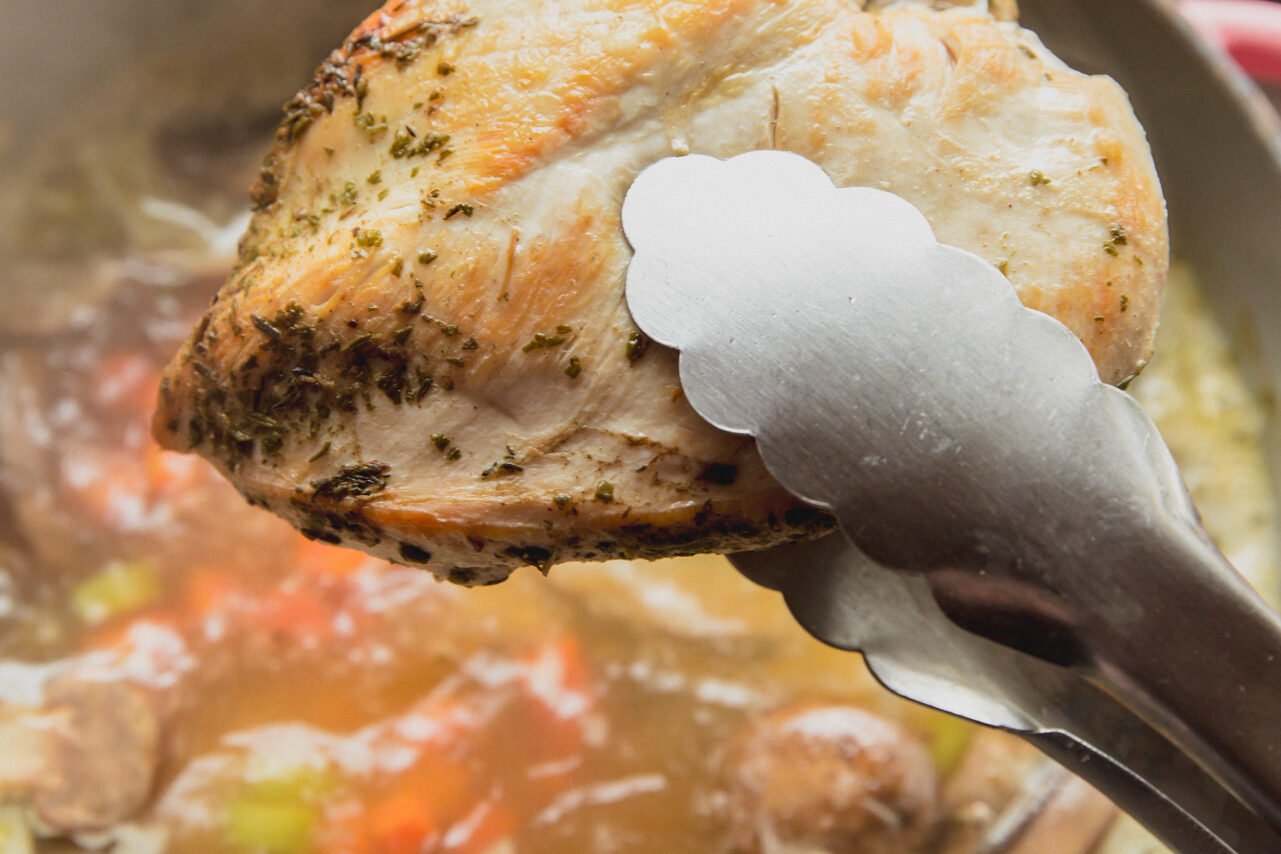 A chicken breast being added to the soup.