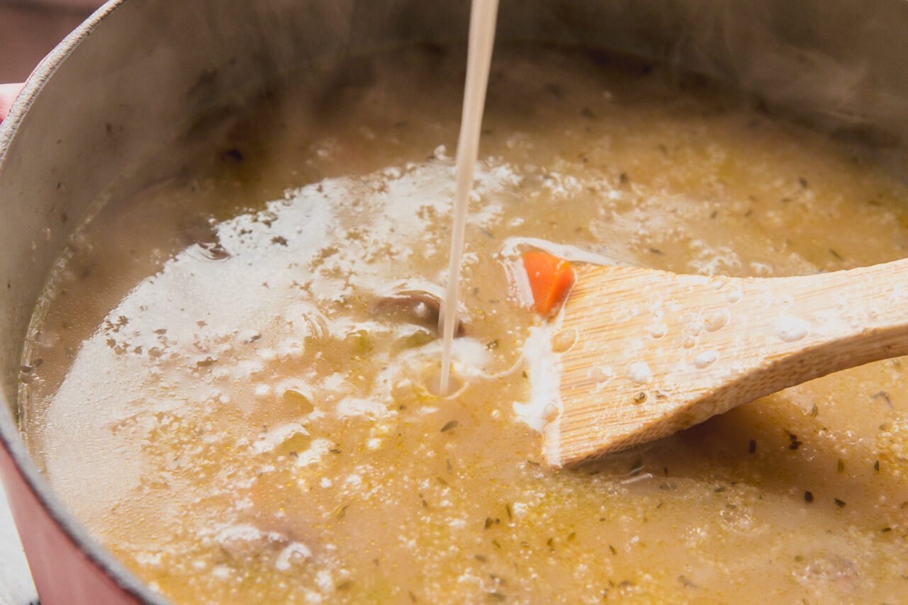 Broth being added to the soup with a wooden soup stiring.